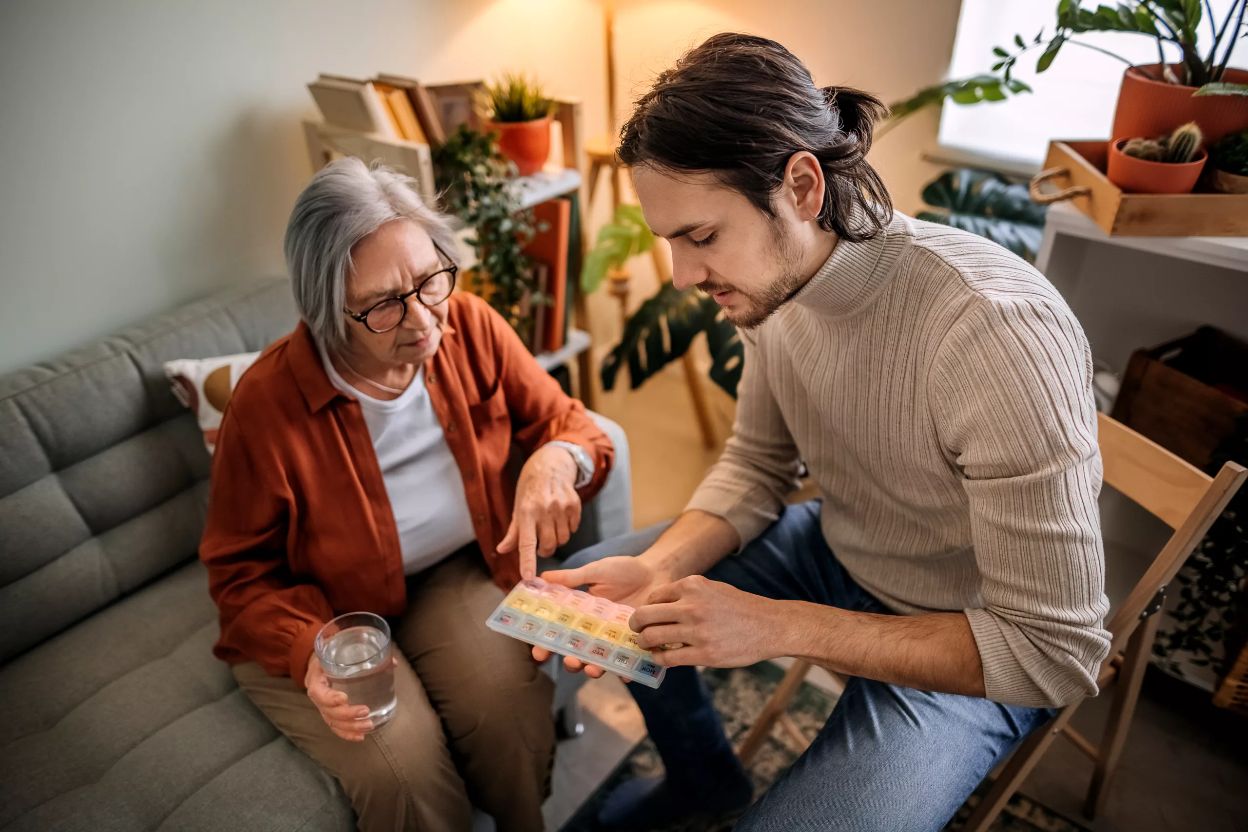 A man assists an elderly woman to take her medication correctly.