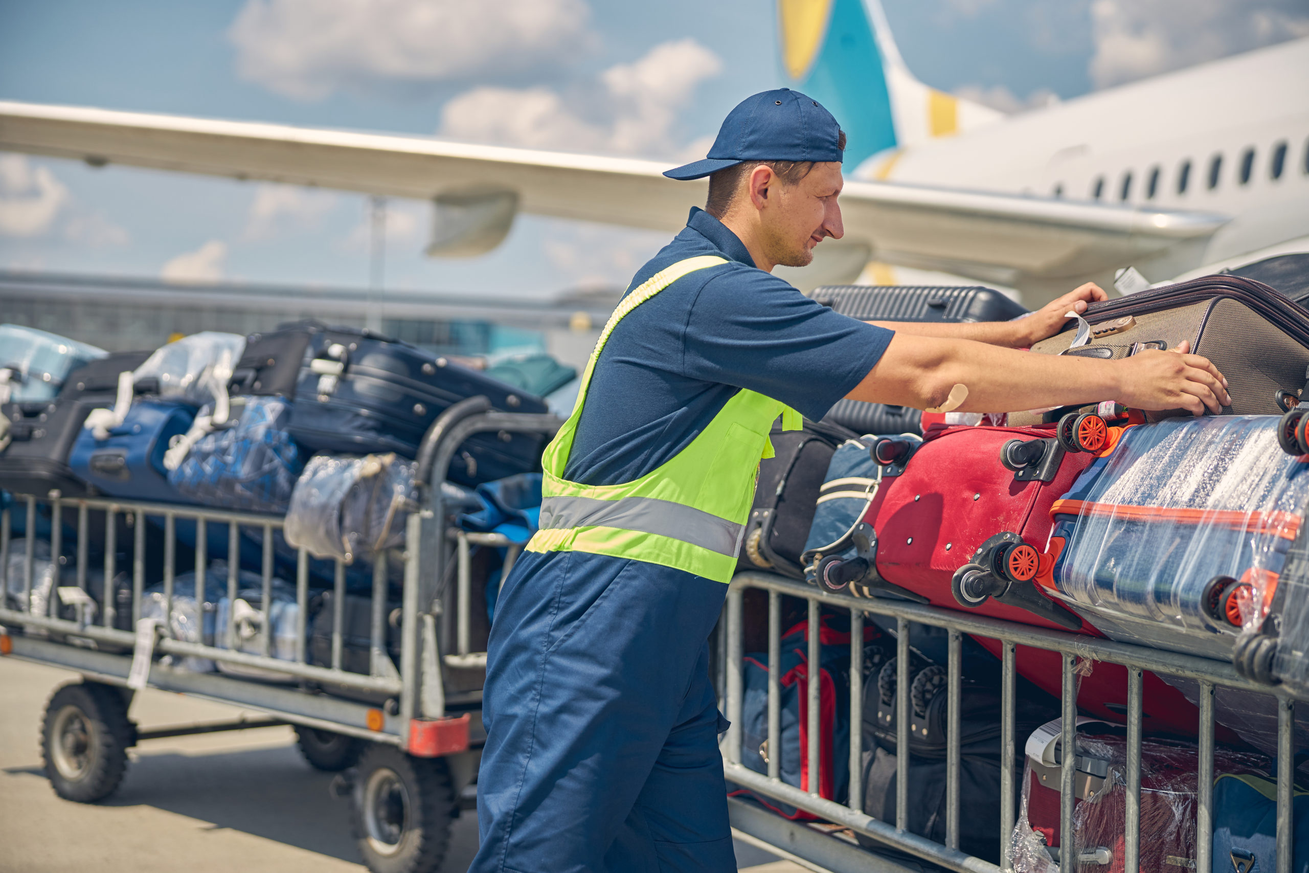 Male airline baggage handler in blue overalls and cap with safety vest, handling luggage