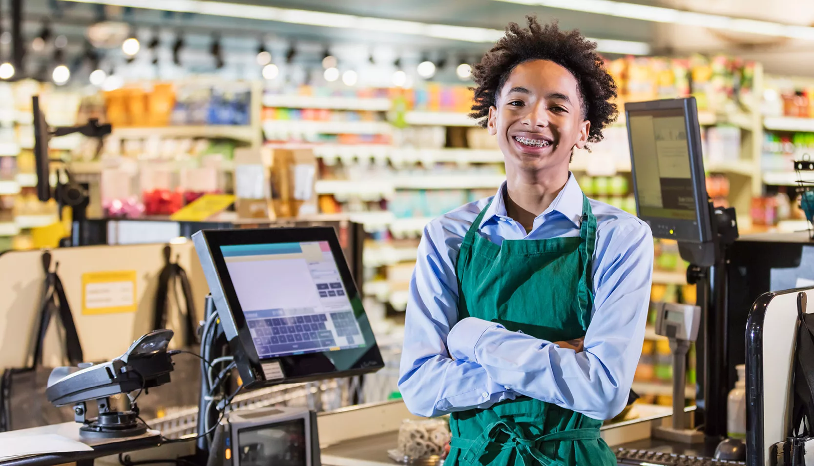 A retail service worker is smiling while standing at a checkout.